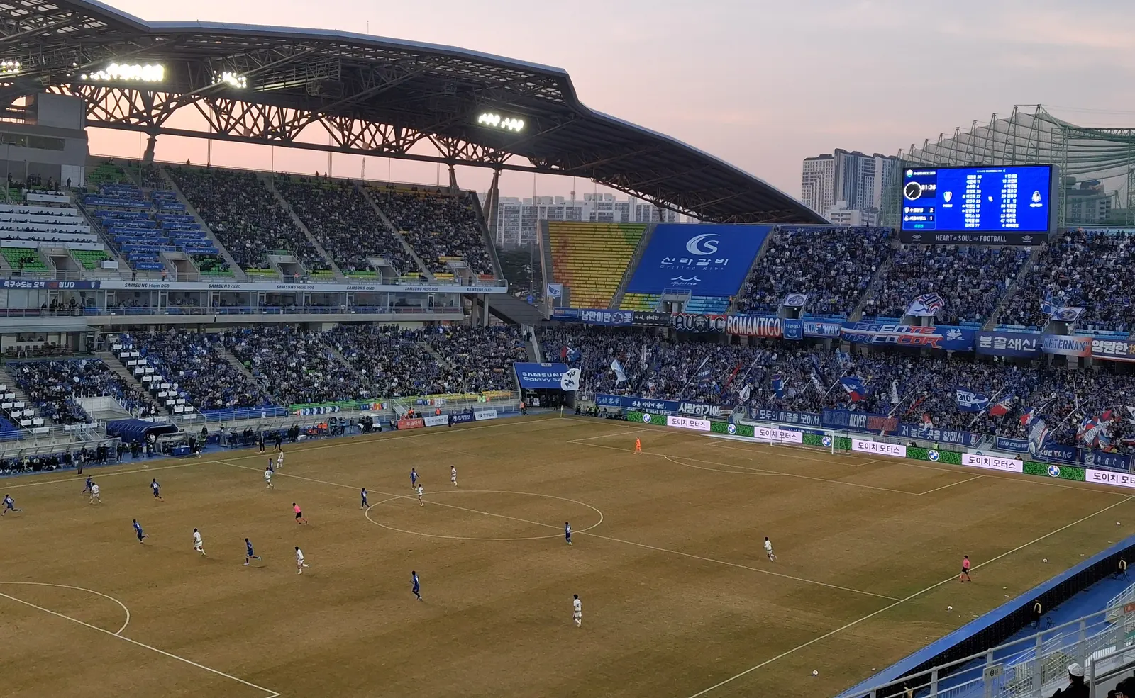 The stands at Suwon World Cup Stadium filled with blue-clad supporters, flags flying and a Frente Tricolor banner across the barrier