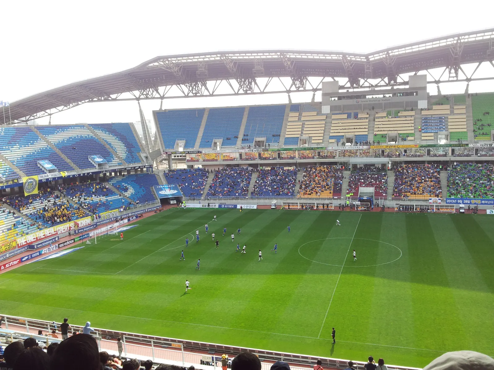 Suwon players in blue during a K League match, the home stand behind them