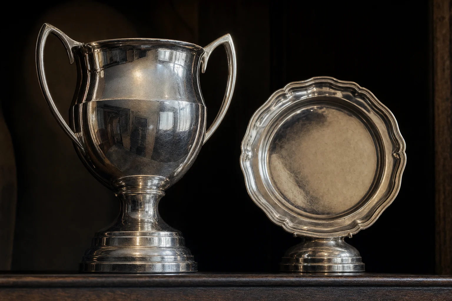 Two plain silver trophies on a dark wooden shelf, lit from the side