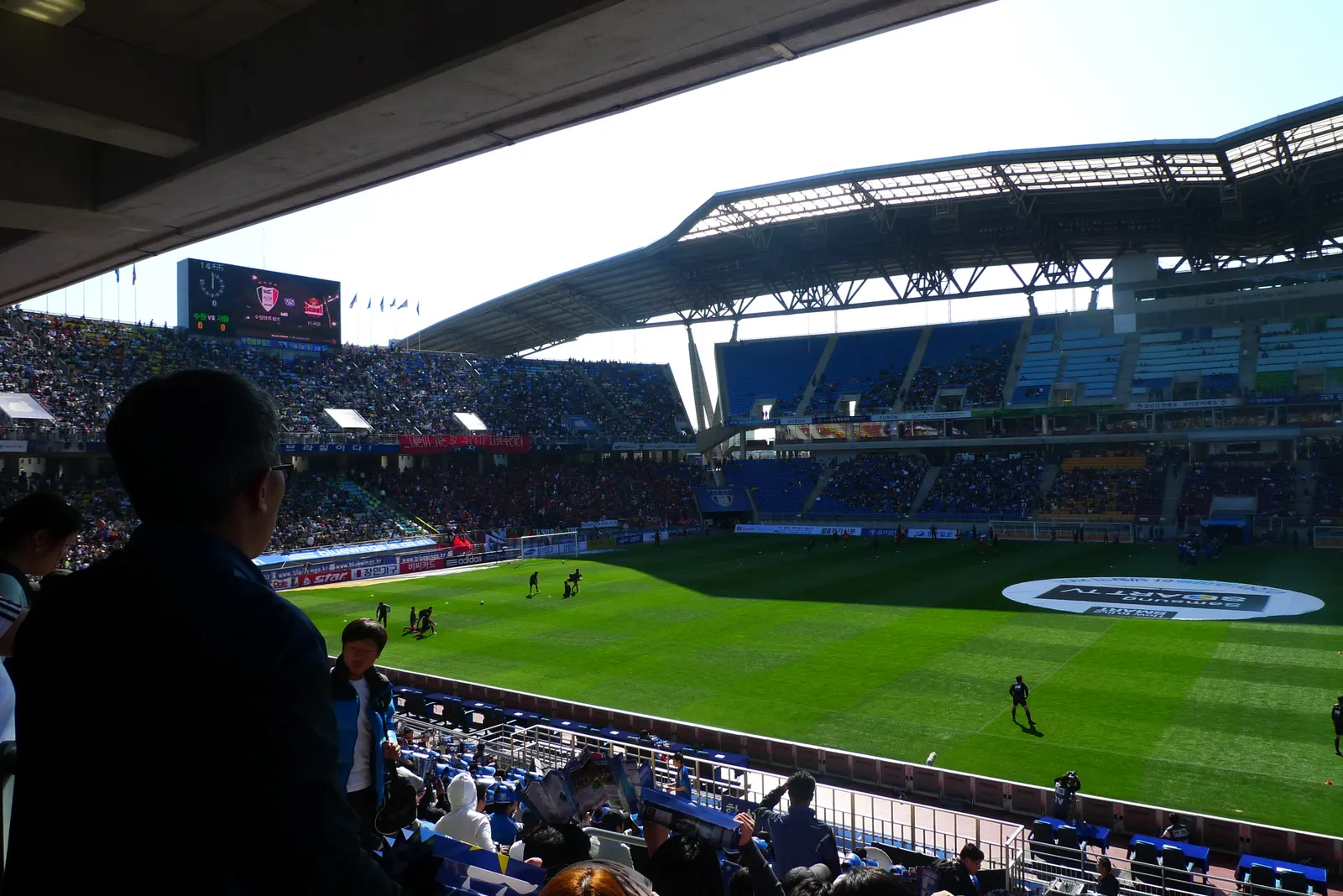 A tier of Suwon World Cup Stadium filled with supporters, the curved roof overhead