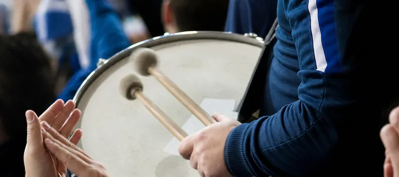 A drum being played in a football terrace, hands clapping around it